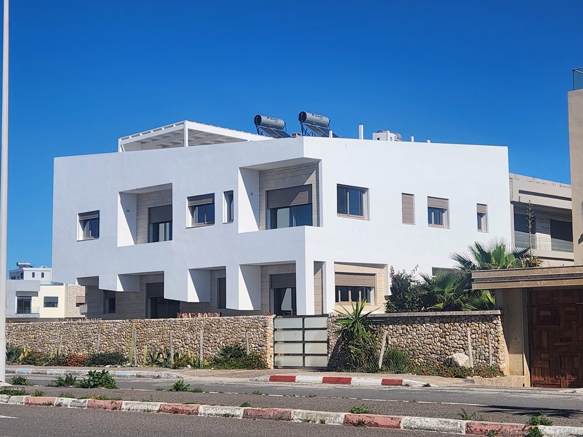 La villa côté rue — blanc architectural, soubassement de pierre, clôture de galets